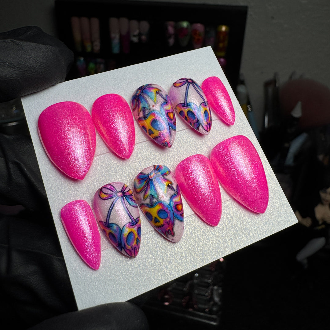 Hot-pink press-on nails with skull and bow accent designs